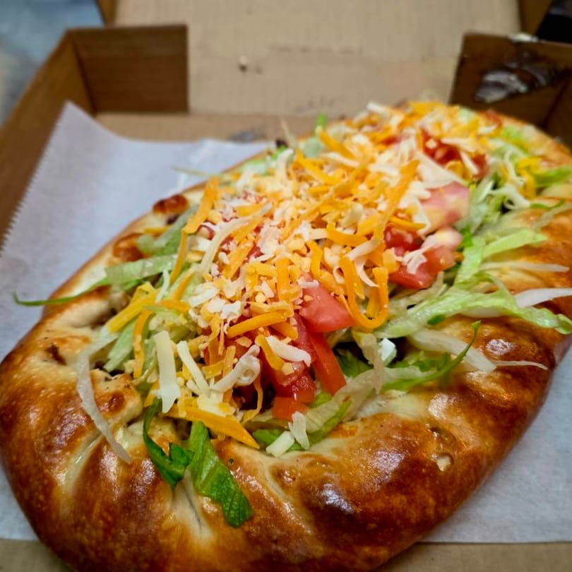 A calzone from Buona Cucina Italiano, topped with shredded lettuce, diced tomatoes, and cheese.