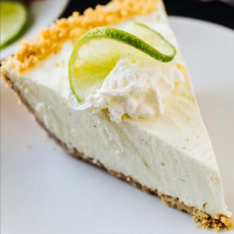 A slice of creamy key lime pie with whipped cream and lime slices on a white plate.