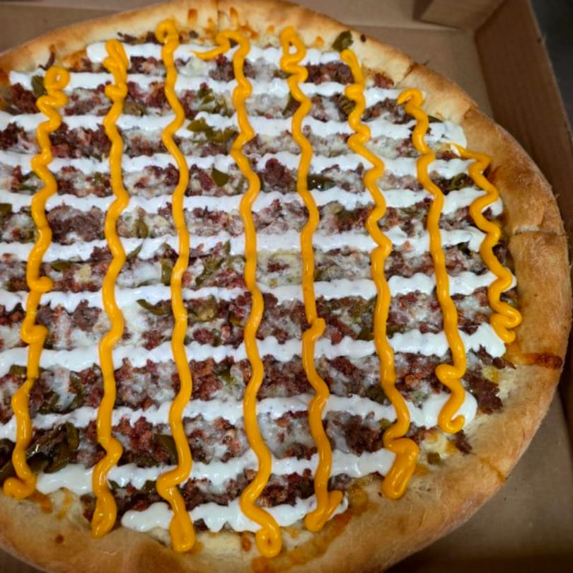Buona Cucina Italiano pizza with white and yellow sauce drizzled over meat and green peppers.